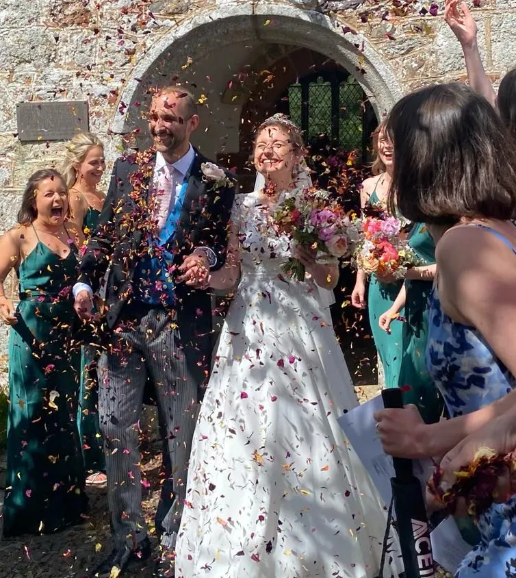 A man and woman couple just married with confetti being thrown over them outside a church surrounded by friends and family