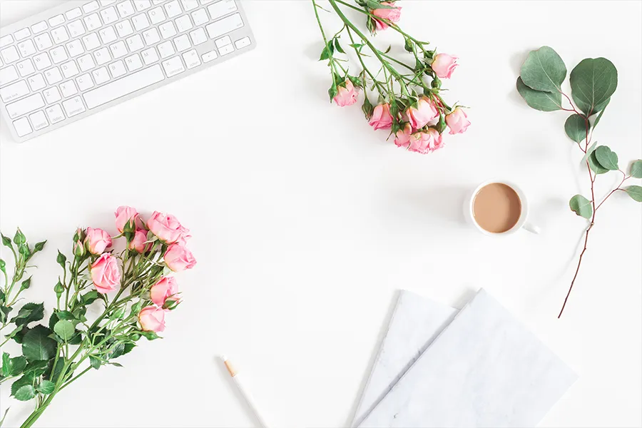 A computer keyboard and flowers on a white background with a cup of tea and notepad