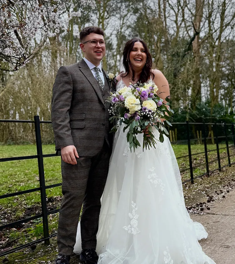 A man and woman just married holding a large bunch of flowers posing for a photograph